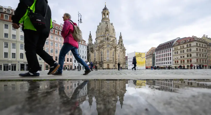 Menschen spazieren über einen nassen Platz vor der Frauenkirche, ein Symbol für offene Kirchen.