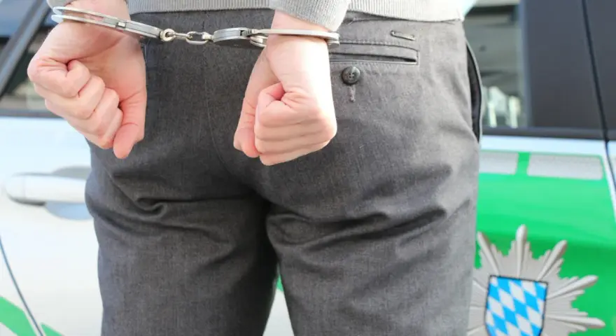 Ręce w kajdankach za plecami, obok radiowozu. Tak wygląda sytuacja, gdy chcesz sprawdzić, jak sprawdzić czy ktoś został zatrzymany przez policję.