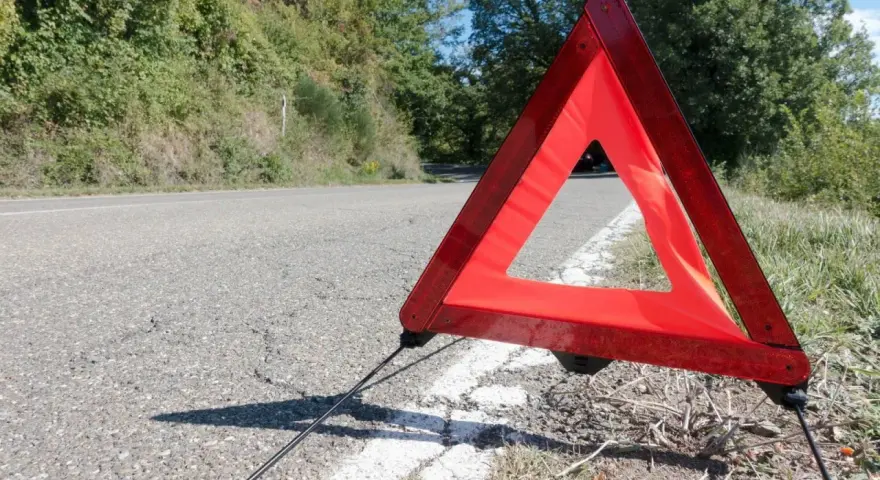 Czerwony trójkąt ostrzegawczy odległości stoi na poboczu drogi, sygnalizując awarię.