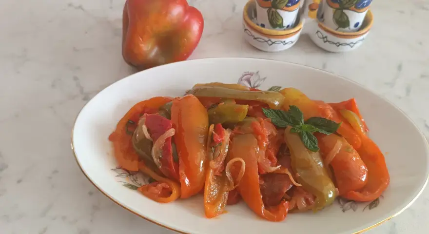 Piatto di peperoni alla siciliana, colorati e saporiti, con un peperone crudo sullo sfondo e saliere decorate.