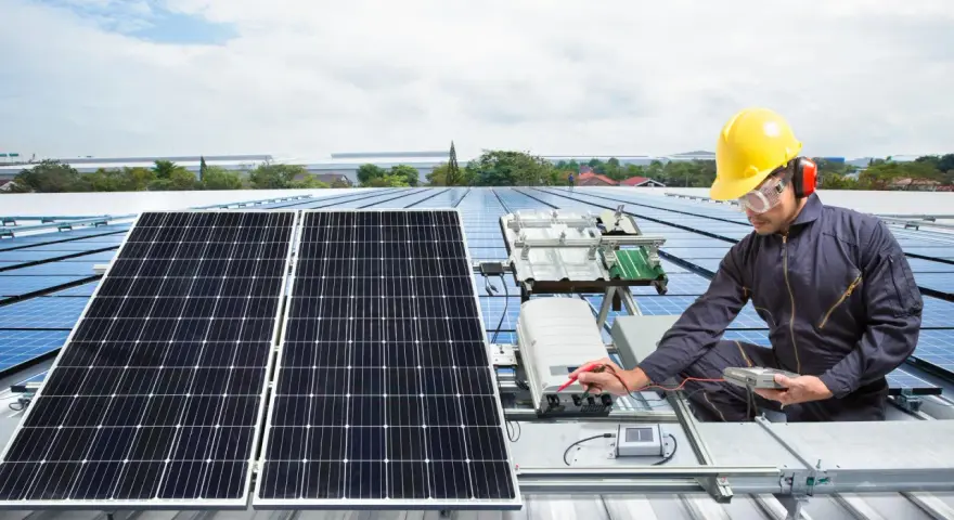 Technik w żółtym kasku sprawdza instalację solar edge na dachu. Panele słoneczne błyszczą w słońcu.