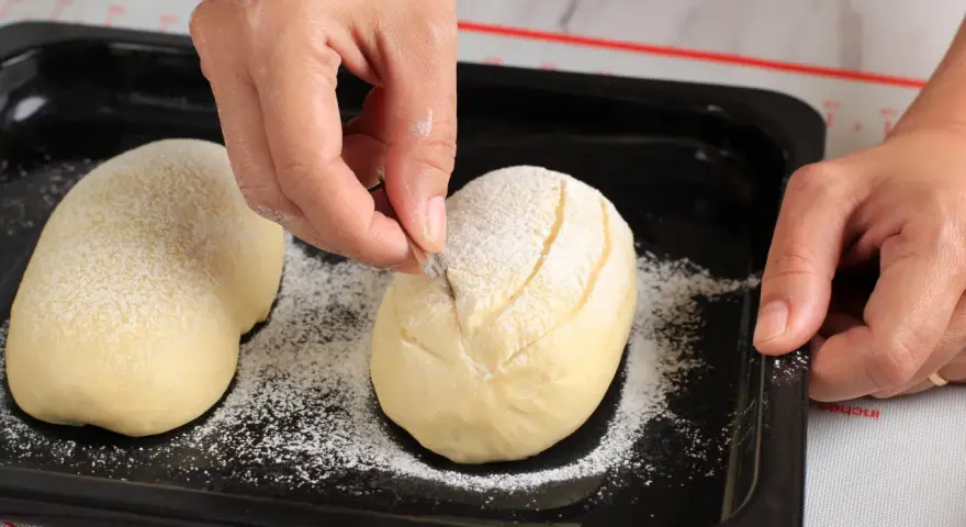 Eine Hand schneidet mit einem Messer Muster in ein mit Mehl bestäubtes Brot.