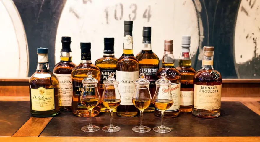 Wybór między single malt czy blended: rząd butelek szkockiej whisky, cztery kieliszki z bursztynowym płynem.