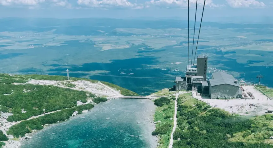 Widok z kolejki linowej na Skalnate Pleso, drugi szczyt w Tatrach. Jezioro, budynek i rozległa panorama.