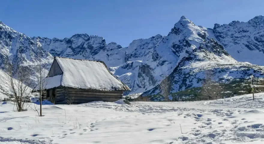 Zimowa hala Gąsienicowa. Drewniana chata kryta śniegiem, otoczona ośnieżonymi szczytami Tatr.
