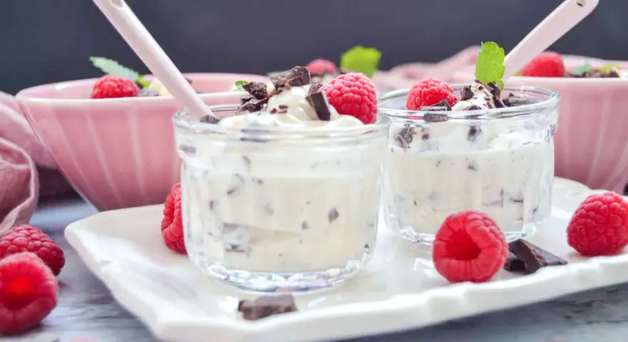Zwei Gläschen mit cremigem Dessert, garniert mit Himbeeren und Schokostückchen. Ein köstliches Herrencreme Rezept zum Genießen.
