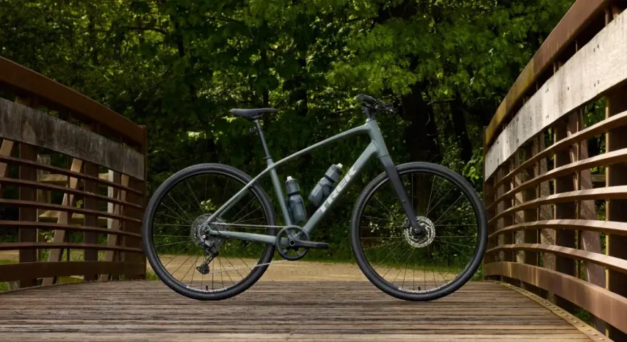 A grey Trek bike sits on a wooden bridge, ready for road or mountain biking adventures through the lush green forest.