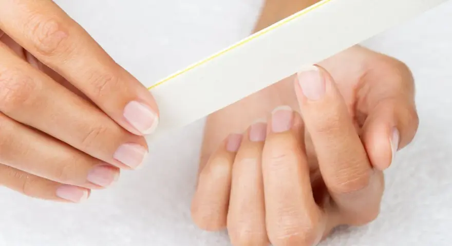 Une main lime délicatement ses ongles, comme un remède de grand-mère pour un ongle abîmé.