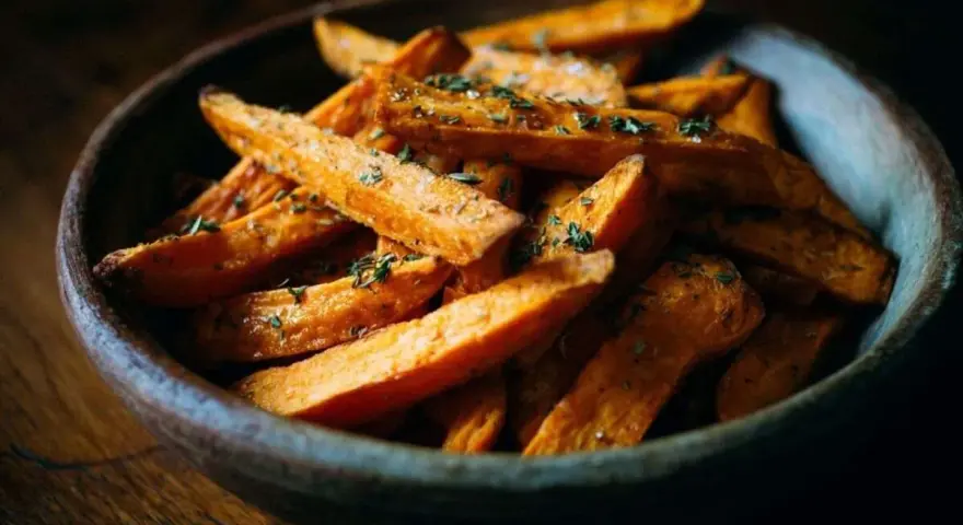 Un bol en bois rempli de frites de patate douce dorées et assaisonnées d'herbes.