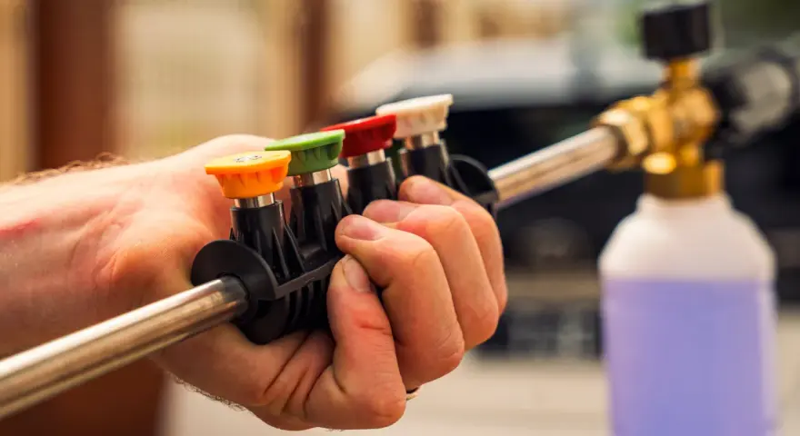 Choosing the right nozzle to pressure wash car is key. This hand holds a selection of colored tips for a pressure washer wand, ready for detailing.