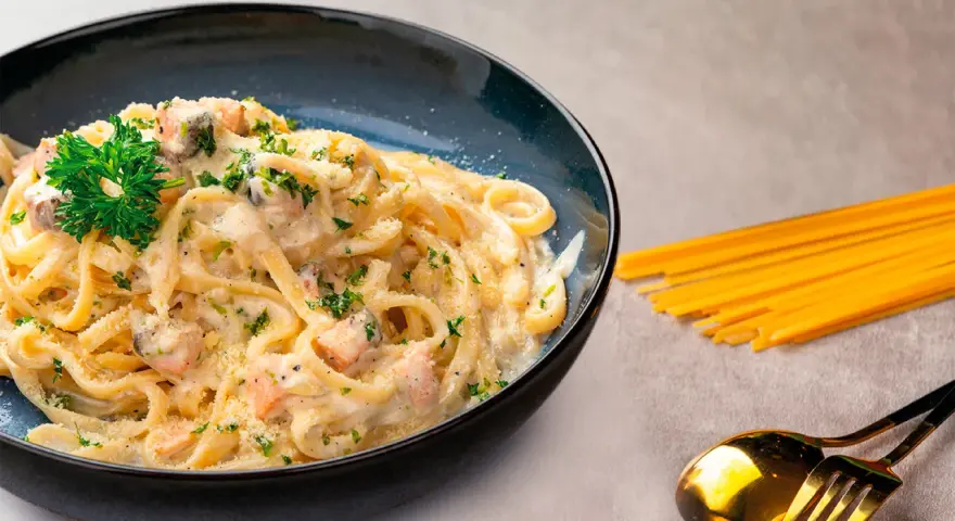 Pasta cremosa con trozos de salmón y perejil, servida en un plato azul oscuro.