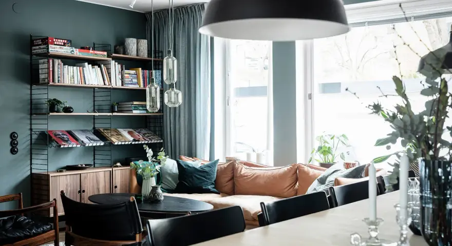 Vardagsrum med 50 tals inredning, bokhylla i svart metall, soffa i läder och stora fönster.