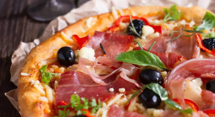 Pyszna pizza z cienko pokrojoną, aromatyczną szynką, czarnymi oliwkami i papryką. Idealna na każdą okazję!