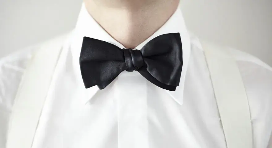 Elegancki mężczyzna w białej koszuli z czarną muszką i białymi szelkami. Kołnierzyk półwłoski idealnie dopełnia stylizację.