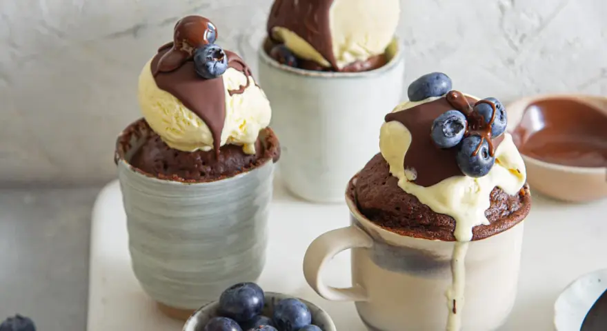 Schokoladiger Tassenkuchen mit Vanilleeis, Schokosauce und Blaubeeren. Ein schnelles Tassenkuchen Rezept für süße Momente.
