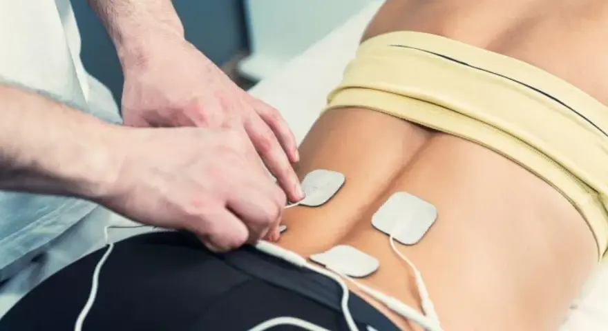 Fysioterapeut applicerar elektroder för elbehandling av muskler i ländryggen.
