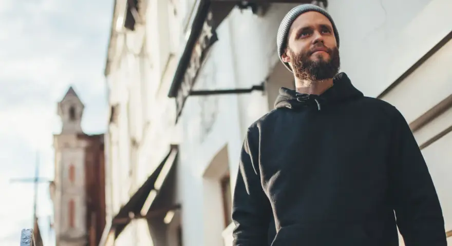 Mężczyzna w czarnej bluzie z kapturem i czapce beanie patrzy w górę. Stylowy sposób, jak nosić bluzę z kapturem.