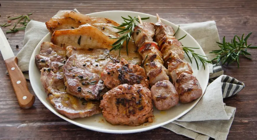 Un piatto invitante di grigliata di carne: costine, spiedini, salsicce e hamburger, guarniti con rosmarino fresco.