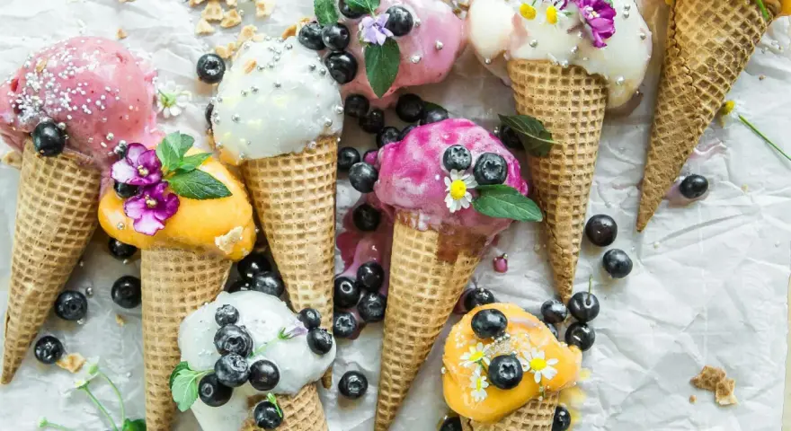 Bunte Eistüten mit Blaubeeren und Blüten. Wer fragt sich, wie viel Kalorien hat eine Kugel Eis, wenn sie so verlockend aussieht?