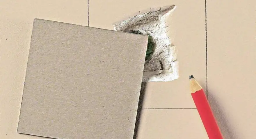 Kartonowy plaster i ołówek czekają, by pokazać, jak załatać dużą dziurę w ścianie.