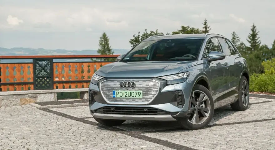 Szary Audi Q4 na kamienistym podjeździe, z widokiem na góry i las.