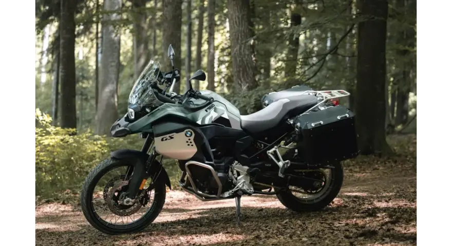 Zielony motocykl BMW F900GS z kuframi, gotowy na przygodę w lesie.