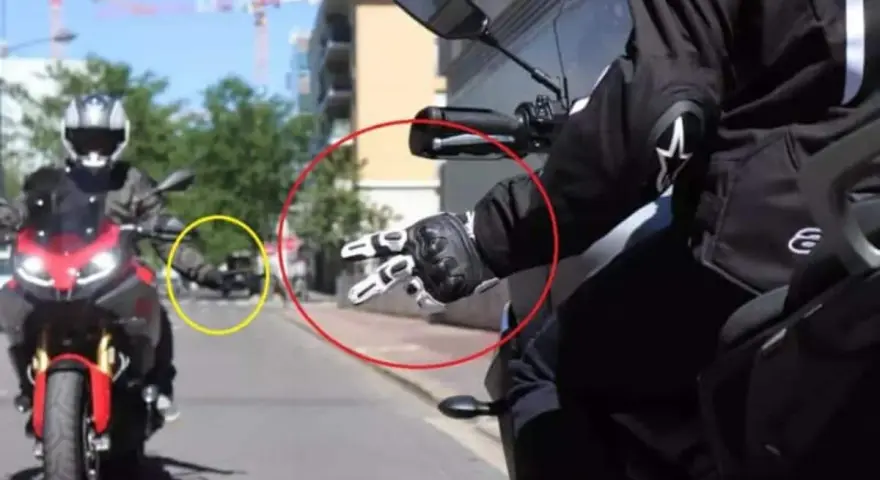 Mano guantata che fa il segno di pace, un gesto del linguaggio motociclisti. Un'altra moto in lontananza.