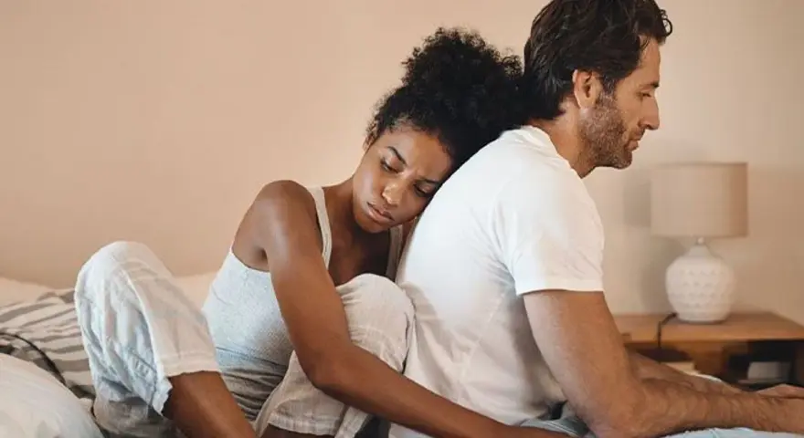 Un couple assis dos à dos sur un lit, l'air distant. On ne peut plus se parler sans s'engueuler.