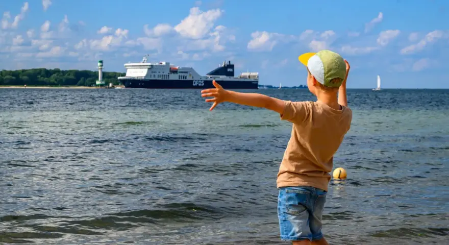 Kind winkt einem großen Schiff in Flensburg zu. Ein toller Ausflug mit Kindern, auch wenn es mal regnet.