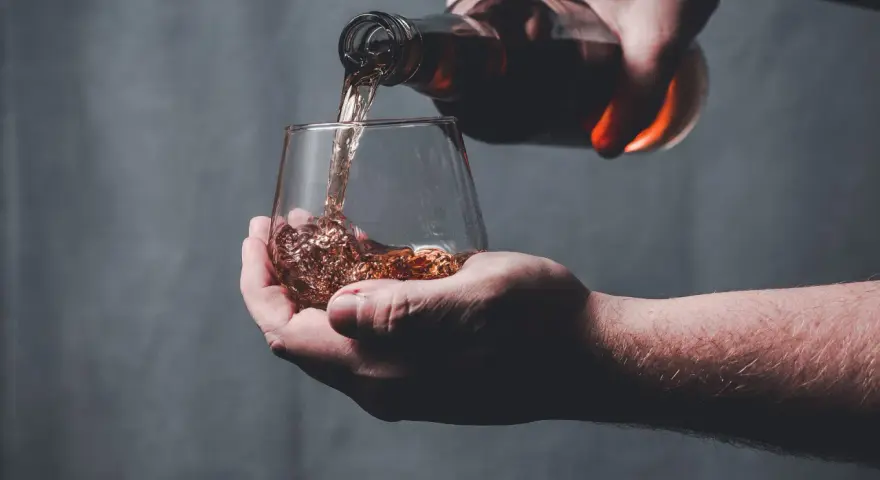 Dłoń nalewa bursztynowy płyn z butelki do szklanki. Czy whisky to bimber?