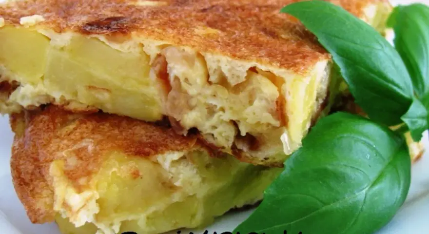 Pyszna tortilla de patatas, ze złotobrązową skórką i soczystym wnętrzem, ozdobiona świeżymi liśćmi bazylii.