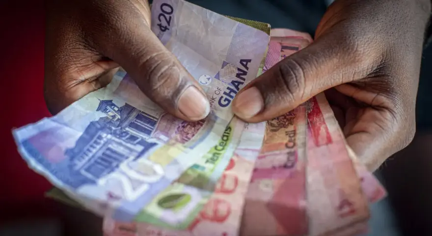 Dłonie trzymające banknoty cedi Ghany o różnych nominałach.