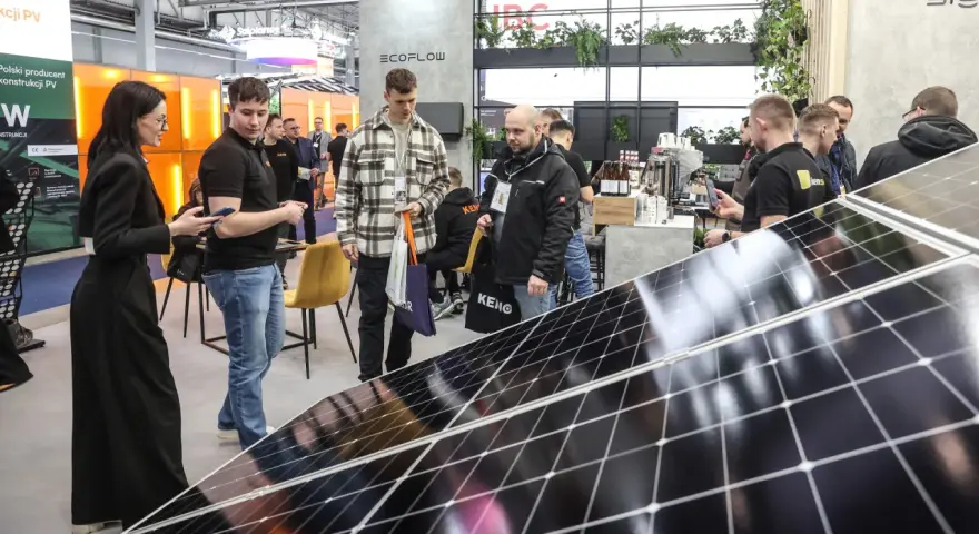 Ludzie zwiedzają targi energii odnawialnej, oglądając panele słoneczne i stoiska firm.