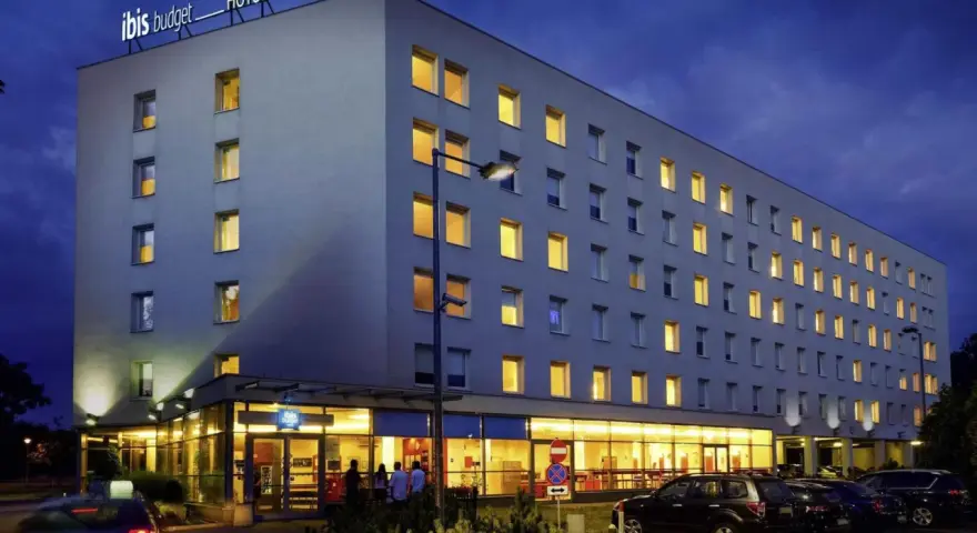 Ibis Budget Warszawa Centrum nocą. Hotel z podświetlanym logo, oknami i parkingiem.