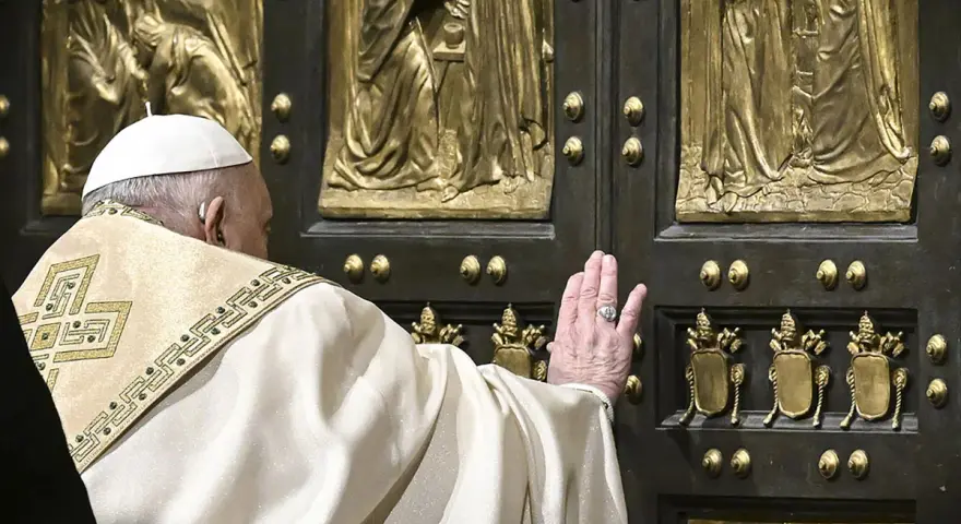 Papst Franziskus berührt die heilige Pforte des Petersdoms. Die bronzene Tür ist mit Reliefs verziert, die biblische Szenen darstellen.