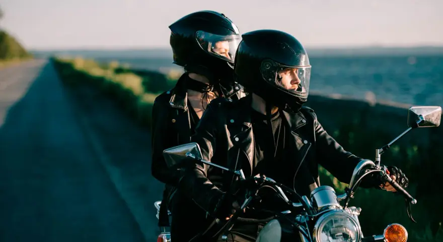Coppia in moto romantica, con caschi neri, giacche di pelle, su una strada panoramica al tramonto.