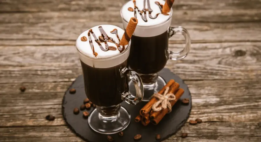 Dwa Irish coffee z bitą śmietaną, polewą czekoladową i laską cynamonu. Jaki to smak? Słodki, kawowy, z nutą alkoholu i przypraw.