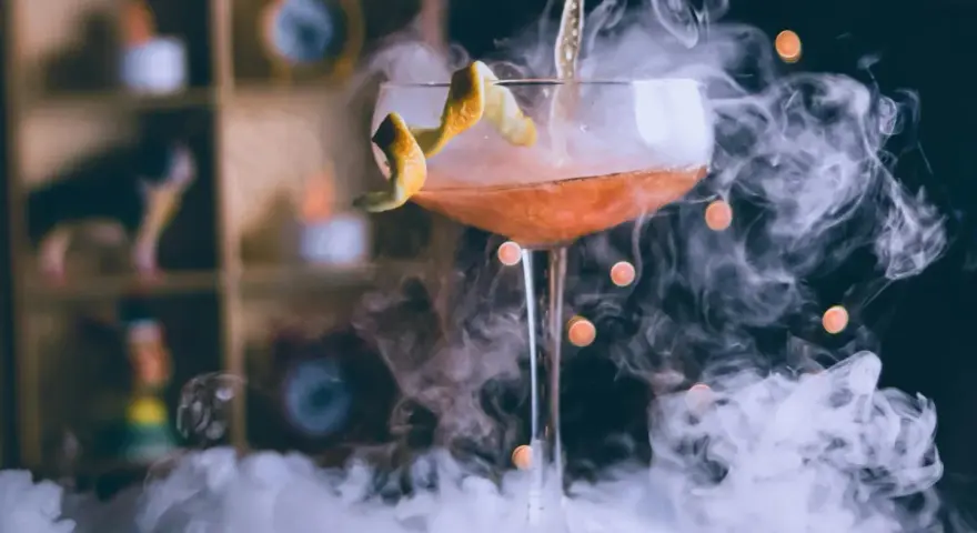 Dymiący drink przepis: koktajl w kieliszku z pomarańczową skórką, otoczony mgłą.