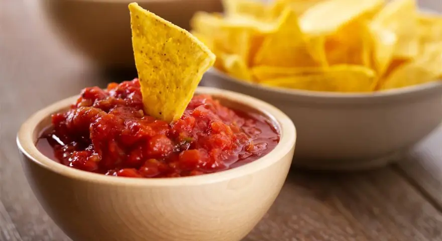 Una tortilla croccante affonda in una ciotola di fresca salsa messicana per tortillas, con altre tortillas sullo sfondo.