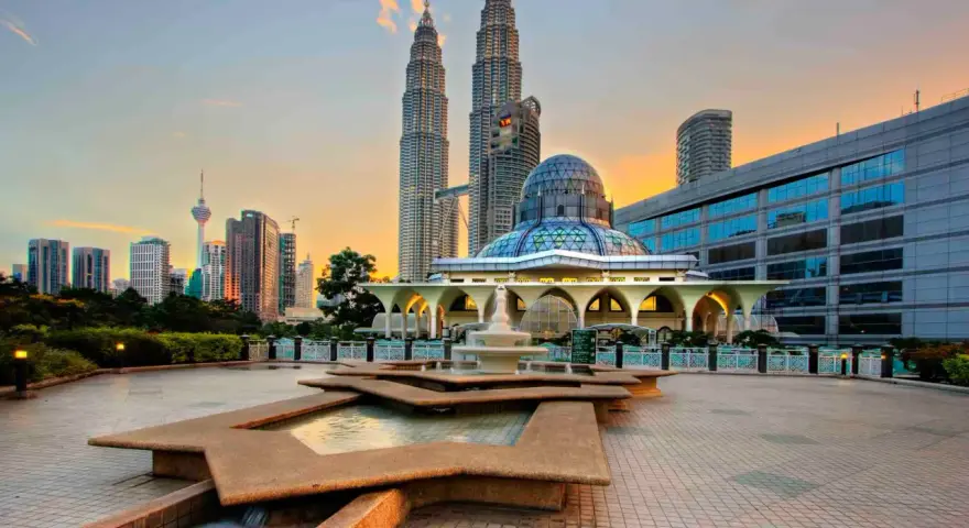 Le Petronas Towers dominano lo skyline di Kuala Lumpur, con una moschea moderna e fontane in primo piano. Un'ottima vista di cosa vedere a Kuala Lumpur al tramonto.