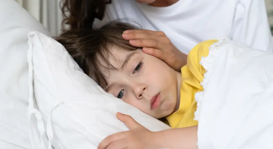 Chore dziecko w łóżku, mama głaszcze je po czole. Warto pamiętać o odpowiednich paracetamol czopki dawki dla dzieci.