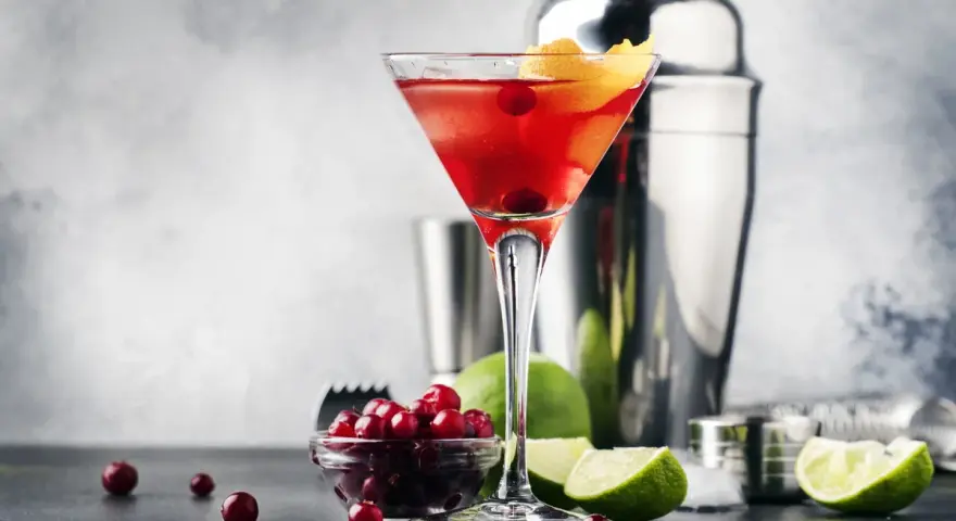 Elegancki cosmopolitan drink, gdzie zamiast żurawiny użyto świeżych owoców. Obok kieliszka stoją limonki i shaker.