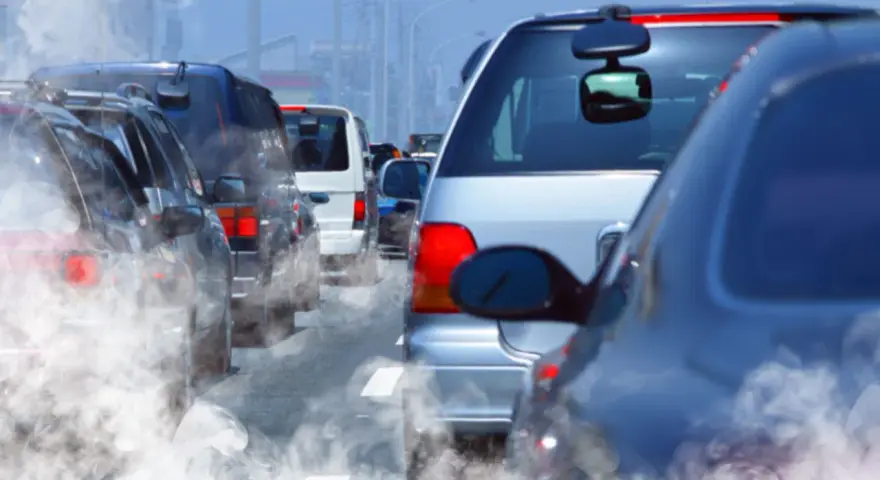 Tráfico denso con humo saliendo de los coches, reflejando la contaminación.
