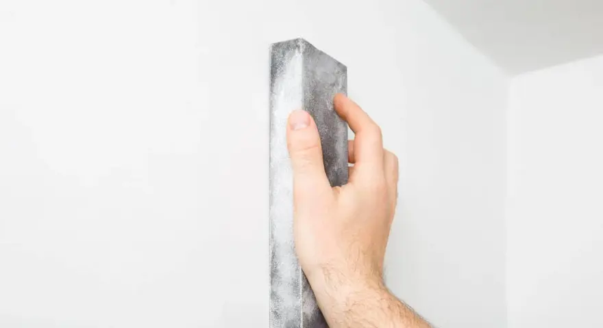 Mano lijando una pared blanca para reparar grietas en techo de yeso.