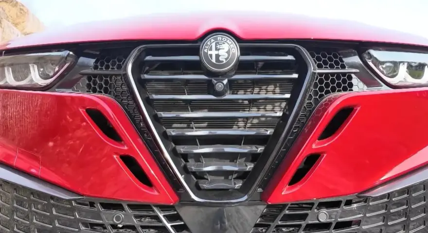 Czerwona Alfa Romeo z bliska. Widoczny grill w kształcie tarczy z logo, reflektory i detale karoserii w zbliżeniu. Alfa makro.