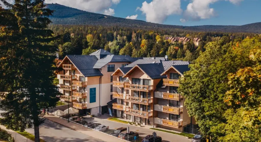 Nowoczesny hotel z drewnianymi balkonami w otoczeniu jesiennego lasu. Idealne noclegi Szklarska Poręba dla miłośników gór.