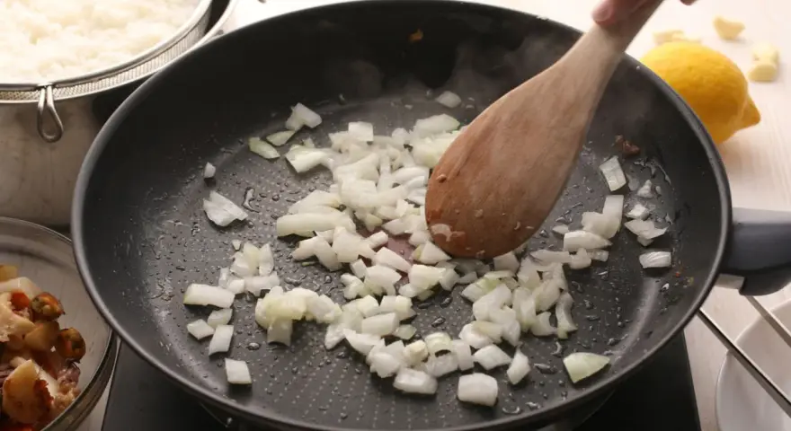 Cebolla picada se sofríe en una sartén, parte de unas deliciosas recetas con cebolla. Arroz blanco y mariscos esperan.