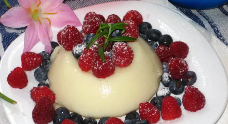Panna cotta z malinami i borówkami, posypana cukrem pudrem. Idealny legumina przepis na deser.