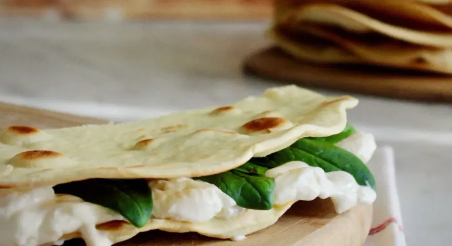Piadina fatta in casa ripiena di mozzarella filante e spinacini freschi, pronta per essere gustata.
