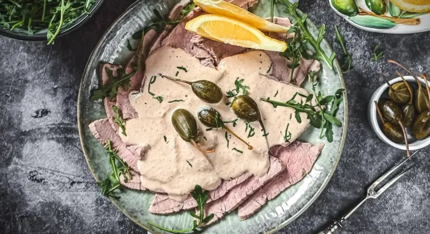 Vitello Tonnato Rezept Original Italienisch: Dünne Kalbfleischscheiben mit cremiger Thunfischsauce, Kapern und Zitronenspalten auf einem Teller.